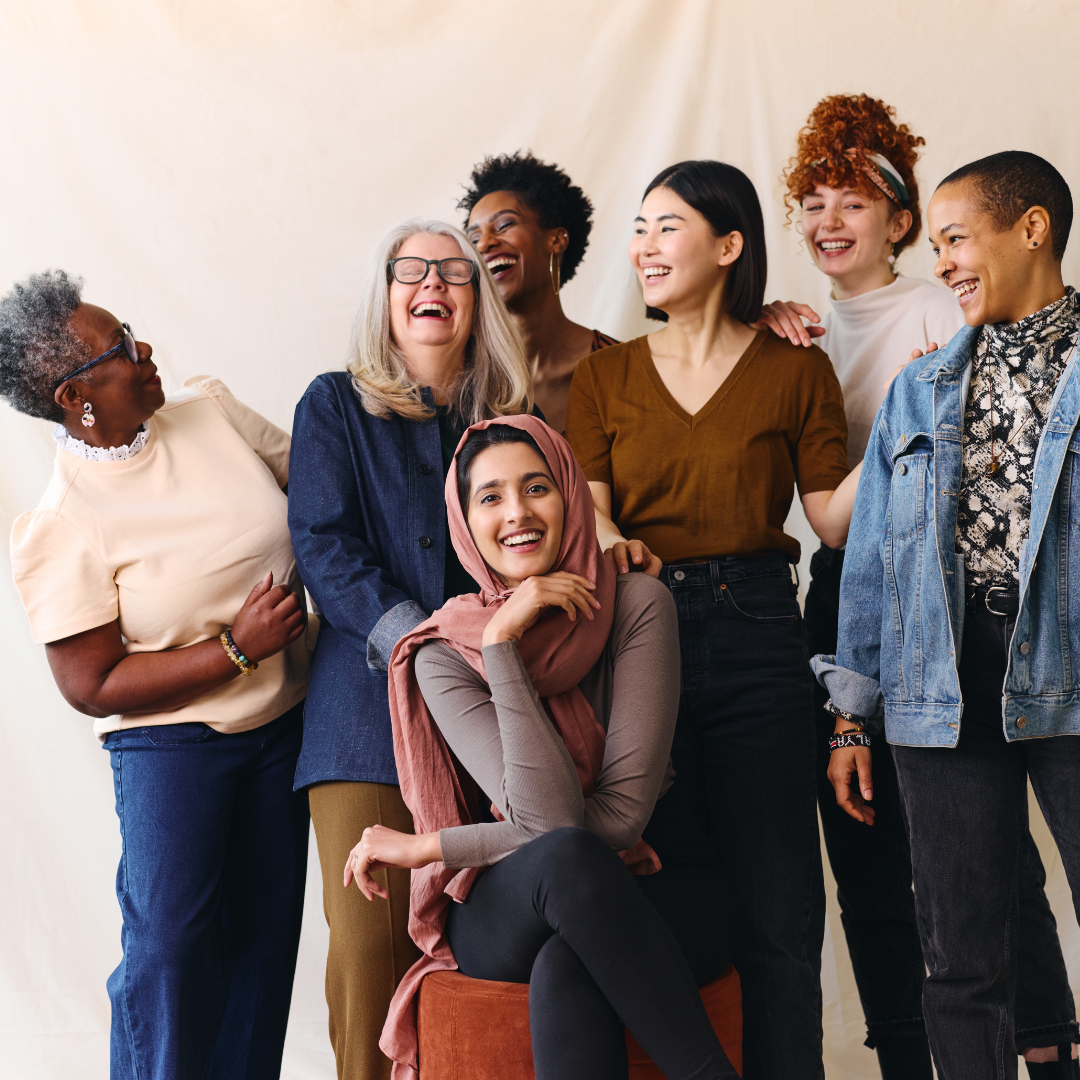A diverse group of six smiling women of different ethnicities and ages posing together.