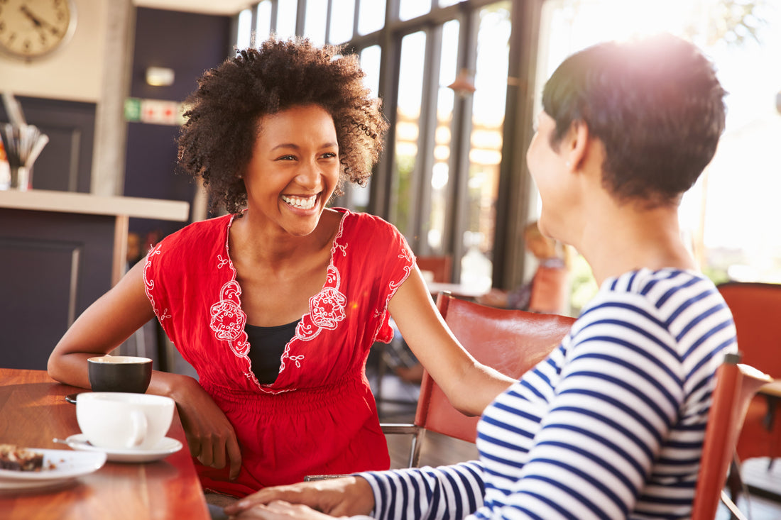 Two women smiling and talking over coffee in a bright cafe.