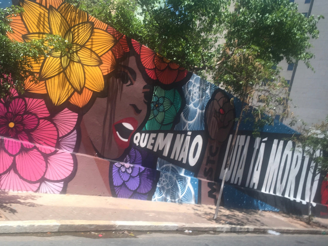 Colorful street art mural of a woman's face with large floral patterns and Portuguese text.