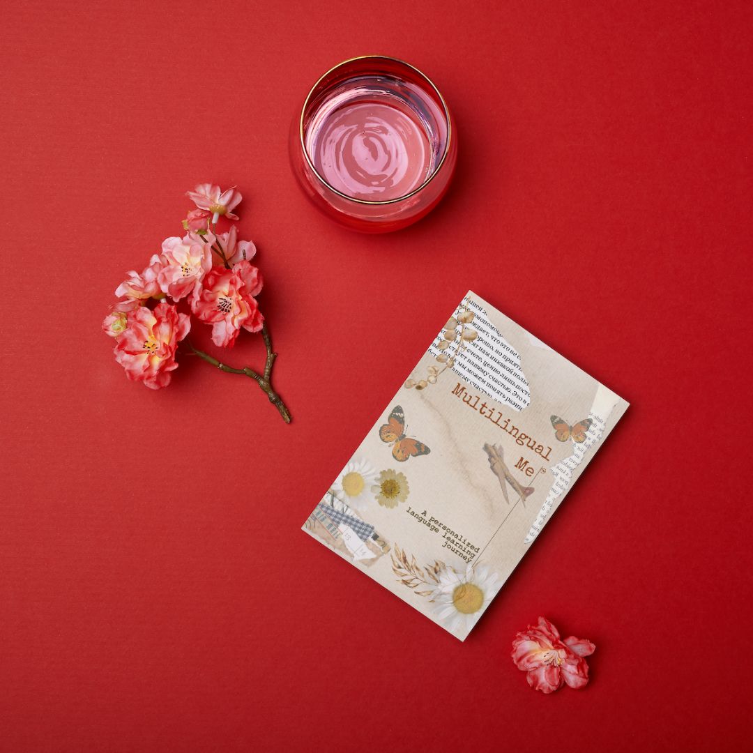 A Multilingual Me language journal on a red background with pink blossoms and a glass of water.