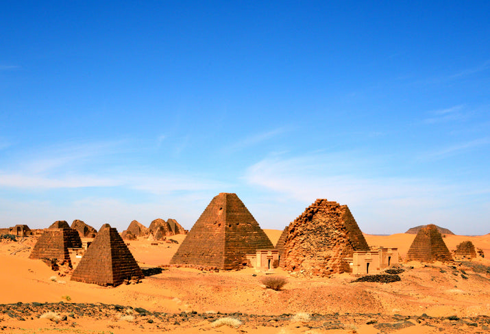 Ancient Nubian pyramids standing in the orange sands of a vast desert under a clear blue sky.