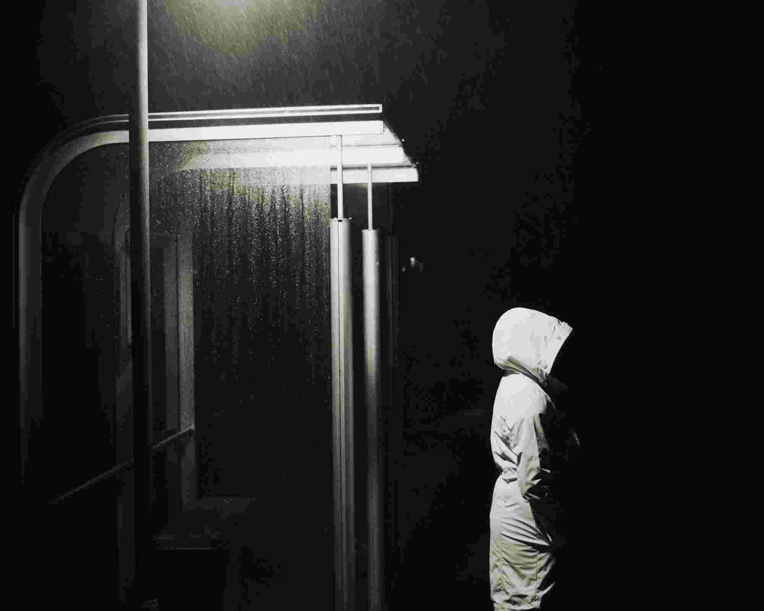 Person in a white hooded raincoat standing beside a lit bus shelter during a rainstorm at night